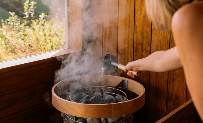Person putting water on hot stones in sauna at Welsh Lavender
